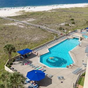View of the pool area featuring a large swimming pool, lounge chairs, and umbrellas, with the beach visible in the background