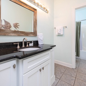 Master bathroom featuring a sleek black countertop, stylish mirror, and a tub/shower combo behind a green curtain