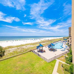 Expansive beachfront view showcases a serene beach, vibrant blue waters, and a welcoming pool area with shaded cabanas