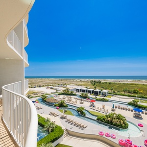 Enjoy breathtaking views from the balcony overlooking lush landscaping and a sparkling pool area under a bright blue sky