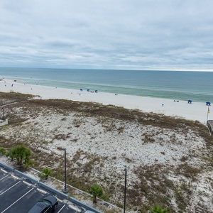 Enjoy a serene view of the pristine beach and calm waters, with a pool visible below for relaxation and fun