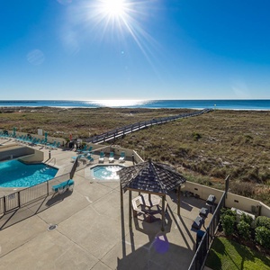 Inviting pool area with turquoise loungers, shaded gazebo, and a scenic path leading to the beach and sparkling gulf waters