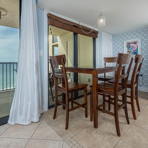 Bright dining area with a wooden table, high chairs, and a breathtaking view of the tranquil waters beyond the balcony