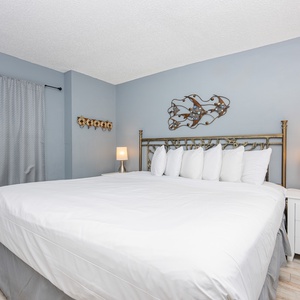 The master cozy bedroom features a large bed with plush white pillows, soft gray walls, and a stylish lamp for a relaxing stay