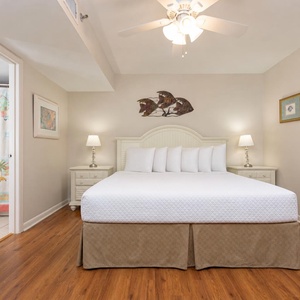 Bright bedroom featuring a king bed with decorative pillows, nightstands, and a doorway leading to a colorful bathroom