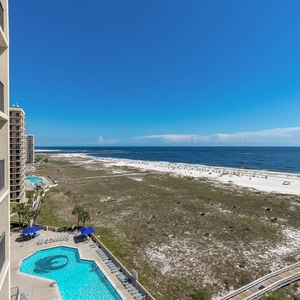 Balcony view showcasing the pool area, lush greenery, and the expansive beach with white sand along the Gulf shoreline