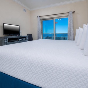 This bedroom features a cozy bed, a TV for entertainment, and a stunning view of the beach through large sliding doors