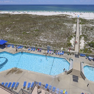 Vibrant pool area with lounge chairs and umbrellas, leading to a boardwalk that connects to the beach