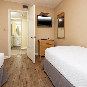 Cozy guest bedroom featuring two twin beds, a flat-screen TV, and an inviting view into the adjoining bathroom