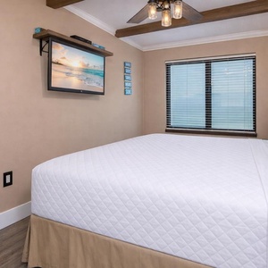 Inviting master bedroom featuring a large king bed, a mounted TV, and inviting natural light from the beachfront window