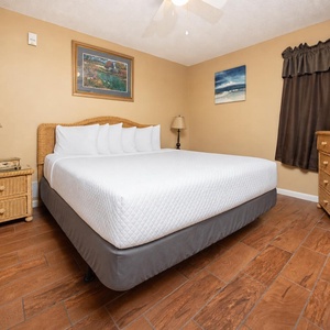 Cozy bedroom featuring a king bed, wicker furniture, and a flat-screen TV, complemented by warm, inviting decor