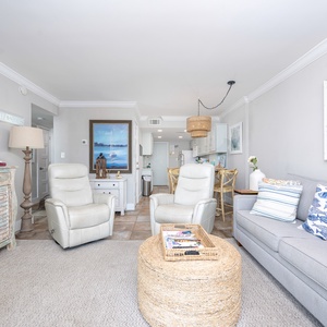 Cozy living area featuring cozy seating, beach-themed decor, and a view into the modern kitchen
