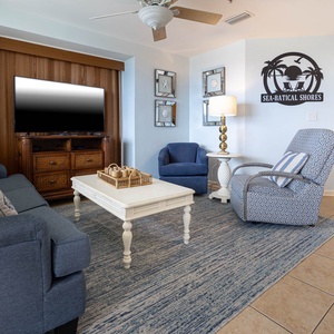 The living area features a cozy blue sofa with queen sofa, accent chairs, a decorative coffee table, and a wall-mounted TV
