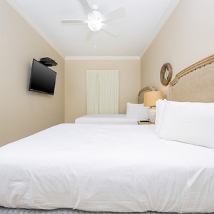 Rest in this guest bedroom featuring two queen beds, a TV, and a window that lets in natural light