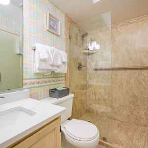 The bathroom features a glass shower, marble accents, and a cheerful pastel tile design, offering a refreshing experience