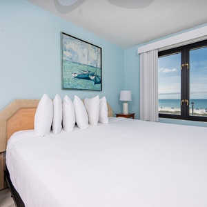 This bedroom features a large bed with fluffy pillows and a stunning beachfront view through the expansive window