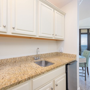 Wet bar with granite countertops, a modern sink, and a glimpse of the stunning coastal view beyond