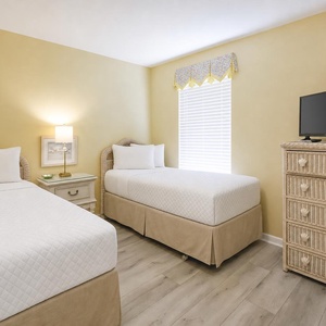 Bright yellow walls complement two twin beds, a TV, and coastal decor, creating a cheerful guest bedroom atmosphere