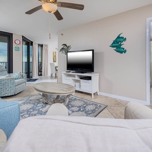Brightly decorated living area features a cozy blue sofa, a patterned armchair, and a view of the beach through large windows