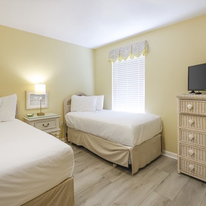 Bright yellow walls complement two twin beds, a TV, and coastal decor, creating a cheerful guest bedroom atmosphere