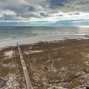 Serene view of the beach with gentle waves lapping against the shore, framed by lush greenery and a wooden walkway
