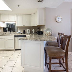 The kitchen features white cabinetry, a granite countertop breakfast bar with seating, and a view into the master suite