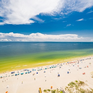 Gaze at the vibrant beach scene below, dotted with colorful umbrellas and sunbathers enjoying the warm sunshine