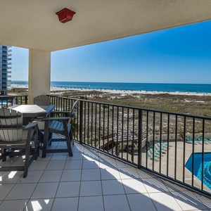 Relax on the balcony with a dining set, overlooking the beach and the inviting pool area, perfect for enjoying the view