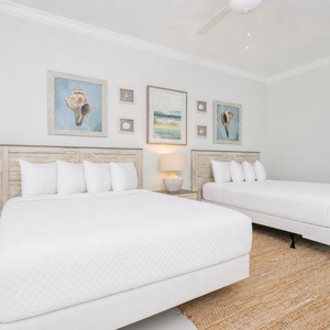 Rest in this guest bedroom featuring two double beds, coastal artwork, and soft natural light