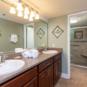 Bright master bathroom featuring dual sinks, decorative palm tree mural, and a walk-in shower with glass enclosure