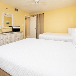 Bright and inviting guest bedroom featuring two comfortable full beds, a TV, and cheerful yellow walls for a cozy retreat