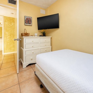 Cozy guest bedroom featuring a white bed, a dresser, and a flat-screen TV against cheerful yellow walls