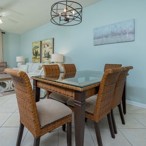 Dine at the glass-top table surrounded by woven chairs, with a view of the beach from the balcony