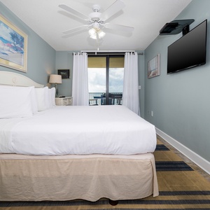 Cozy master bedroom featuring a king bed, wall-mounted TV, and access to a balcony with views of the gulf