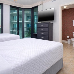 Relaxing guest bedroom featuring two full beds, a flat-screen TV, and a view of the tropical-inspired decor