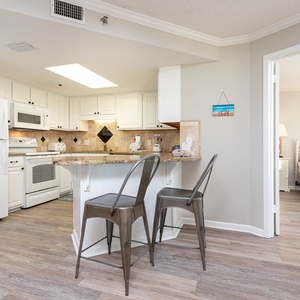 Kitchen area featuring white cabinetry, a granite breakfast bar with metal stools, and a view into the adjacent bedroom