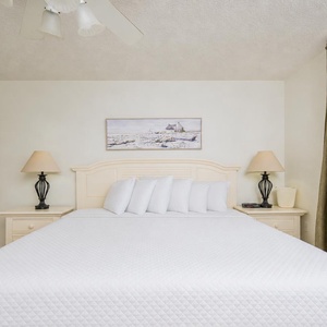 The master suite bedroom featuring a large king bed, bedside lamps, and a view of the beach through sliding glass doors