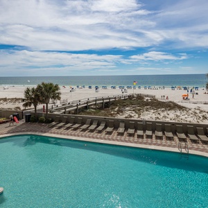 This inviting balcony view showcases a sparkling pool area with lounge chairs, leading to a beautiful beach just steps away