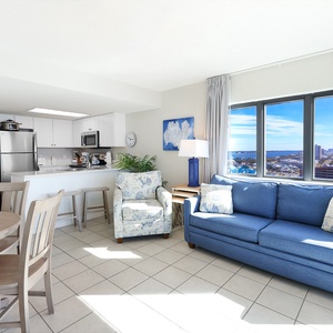 Unwind in the bright living area with a blue sofa, dining table, and large windows that showcase the coastal view