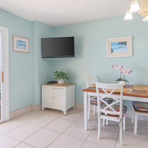 This dining area features a light blue wall, a TV, and a table with a view of the beachfront balcony, perfect for meals