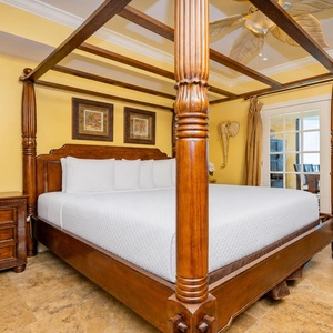 Unwind in the elegant master bedroom featuring a four-poster king bed, warm decor, and a view into the dining area