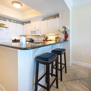The kitchen features white cabinetry, granite countertops, and a breakfast bar with stylish seating