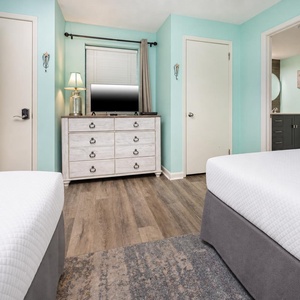 Brightly colored walls complement two double beds and a dresser with a TV, leading to a bathroom area with modern fixtures
