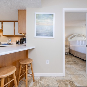 A well-equipped kitchen features a breakfast bar with wooden stools and a glimpse of a serene master suite