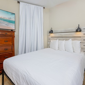 Guest bedroom featuring a queen bed, twin bunk, stylish wooden dresser, and a large TV