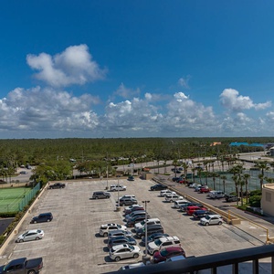 A master balcony view showcases a vibrant landscape with tennis courts and palm trees under a bright sky