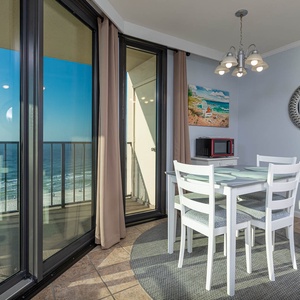 Bright dining area features a round rug, white table with four chairs, and a view of the beach through large glass doors