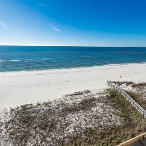 The image showcases a serene beachfront view with soft white sand and gentle waves under a clear blue sky