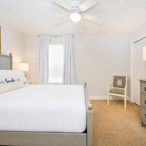 Tranquil guest room featuring a queen bed and a charming coastal painting above the headboard