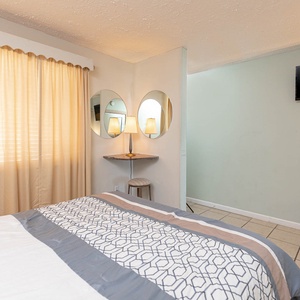 This cozy bedroom features a stylish bed with patterned linens, a TV, and warm natural light from the curtains